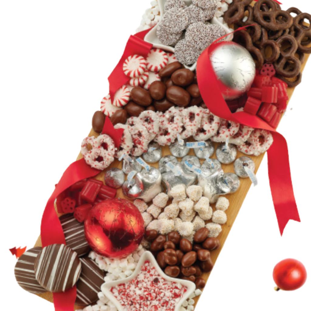 Chocolates and pretzels on a wooden board with holiday ornaments and red ribbon decorating them