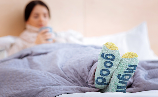 A person is sitting in a bed. She is wearing fuzzy socks that are the focus of the image