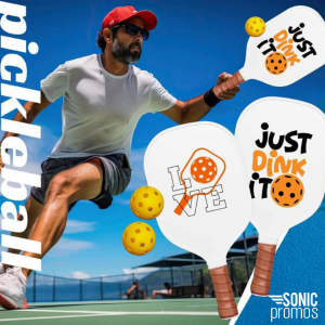 An action image of a man playing pickleball outside. He's holding a custom branded pickleball paddle with a logo on it. In front, two branded pickleball paddles and balls. The text says "pickleball"