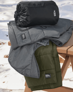 A pile of three folded Eddie Bauer ponchos are sitting on a small wooden table. 
