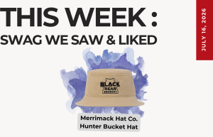 This Week: Swag We Saw & Liked. Beige bucket hat with Black Bear Brewery logo over purple watercolor, with a tag reading Merrimack Hat Co. Hunter Bucket Hat, and a July 16, 2026 badge.